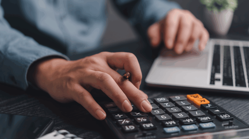 Person using a calculator and laptop with notebook, illustrating commercial property budgeting and financial planning